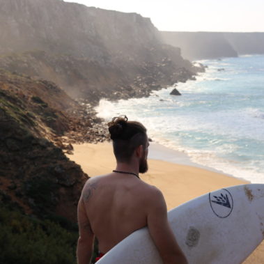 Surfer mit Surfboard unter dem arm blickt aufs Meer von der Steilküste aus